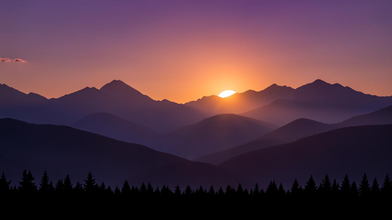 Sun setting between layered mountain ridges under a purple and amber sky
